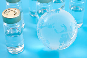 Global vaccines supply, international medical emergency and worldwide vaccination effort concept with glass globe and vaccine doses isolated on blue background