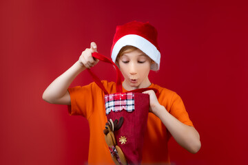 A boy in a Santa's Christmas hat looks into a gift bag