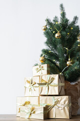a small Christmas tree with warm bulbs in a pot on a wooden table with gifts wrapped in gold paper. the concept of Christmas