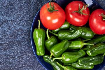 Red tomatoes and green peppers on a blue plate on a piece of slate. Vegan food concept