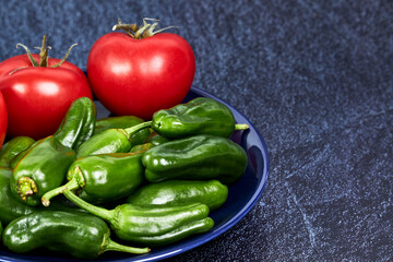 Red tomatoes and green peppers on a blue plate on a piece of slate. Vegan food concept