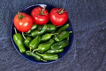 Red tomatoes and green peppers on a blue plate on a piece of slate. Vegan food concept