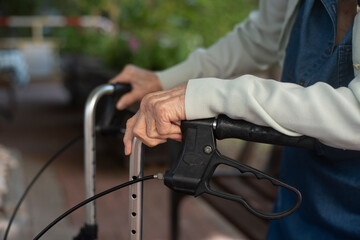 Old person's hands holds at handles modern comfortable walker. Difficult for elderly human to walk without support. Lifestyle of old person. Close-up. Safety for life.