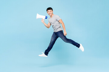 Young happy smiling Asian man holding megaphone jumping in isolated light blue background