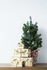 a small Christmas tree with warm bulbs in a pot on a wooden table with gifts wrapped in gold paper. the concept of Christmas