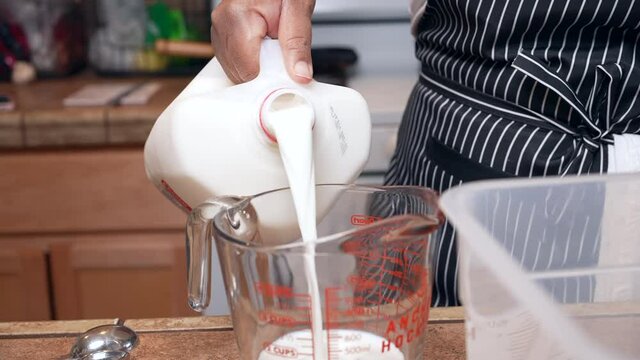 Pouring whole organic milk into a measuring cup for a special, homemade recipe - side view 