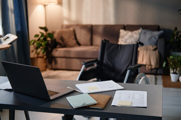 Image of workplace with laptop on it and wheelchair near the table in empty living room