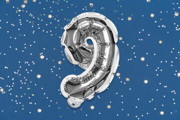 Silver foil balloon number, digit nine on a blue background with sequins. Birthday greeting card...