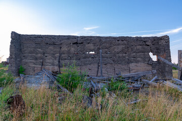 An old gray sullen destroyed wall of a concrete building with rebar outside the city against a blue sky. Close-up