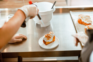 Professional confectioner makes pattern on cake with cream using gas burner at countertop