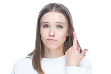 Close up shot of young scared woman pointing with her finger on an applied adhesive bandage on her forehead after injury isolated on white background