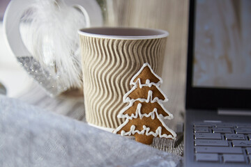 Beige cardboard cup with hot beverage and cookie in shape of Christmas tree. Trendy fluffy decorations. Wooden festive Christmas background. Aesthetic cozy home or office concept