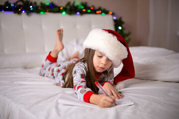 Merry Christmas and Happy Holidays. The little happy girl on the bed wrote a letter to Santa Claus
