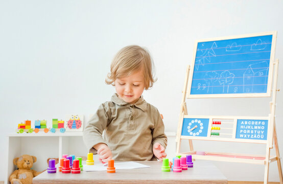Cute little child having fun at home playing with colorful stamps on paper. Indoor activity for kids.