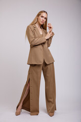 High fashion photo of a beautiful elegant young woman in a pretty beige brown suit, pants unbuttoned at the seam, jacket posing on white background. Studio Shot. Slim figure, wide clothes.