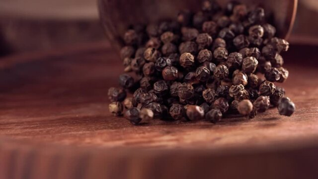 Black pepper falling on a wooden table .Slow motion. Close up