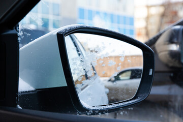 Side mirror of a white new snow-covered car with a reflection covered with frost on a sunny bright frosty day in the Urals. Selective focus. Close-up