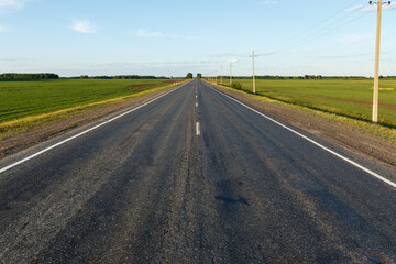 Countryside asphalt road with marking. Electricity pylon along the road.
