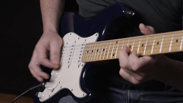 A male musician plays a melody on a blue six-string guitar.