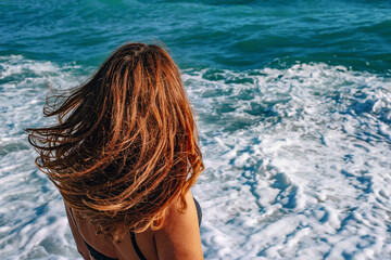 Woman on the beach with beautiful hair. Brunette girl admires the sea. The concept of freedom, well-being and relaxation. 