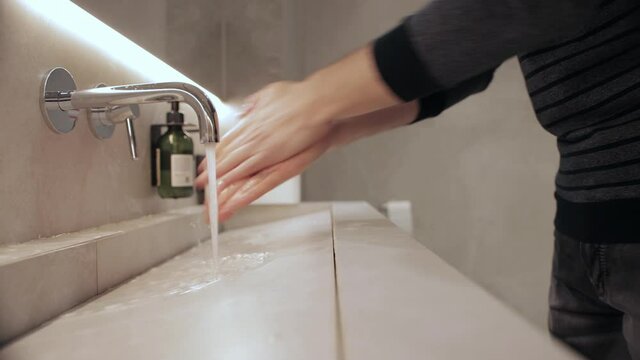 A man washes his hands with liquid soap in a public toilet. Hand hygiene from infection and germs, close-up