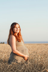 Fototapeta na wymiar beautiful young pregnant woman walks on wheat field at sunset, expectant mother with relax in nature stroking her belly with hand, happy pregnancy concept