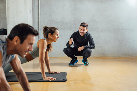 Personal Trainer Encourages people to do push-ups, plank position, in gym.