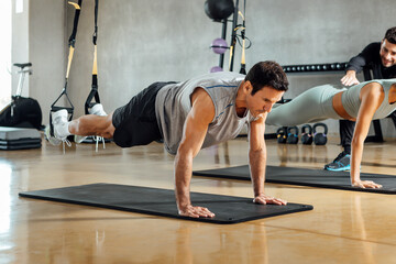 Fototapeta na wymiar Strong man performing plank pose, suspensions training exercise at gym.