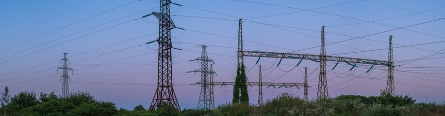 High-voltage power towers and poles with wires in the green grass against a background of...