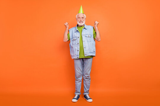 Photo of charming lucky retired man wear vintage jeans waistcoat birthday headwear rising fists smiling isolated orange color background - Powered by Adobe