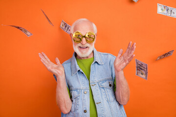Photo of impressed funny retired man wear vintage jeans waistcoat money glasses air wind blowing smiling isolated orange color background