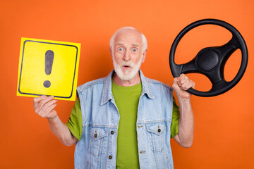 Photo of cute impressed retired man wear vintage jeans waistcoat holding steering wheel stop gesture placard isolated orange color background