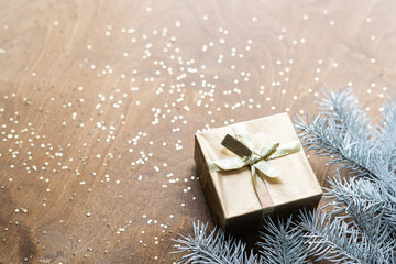 a golden gift box on a wooden table with gold spangles in the shape of stars, among the fir branches