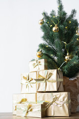 a small Christmas tree with warm bulbs in a pot on a wooden table with gifts wrapped in gold paper. the concept of Christmas