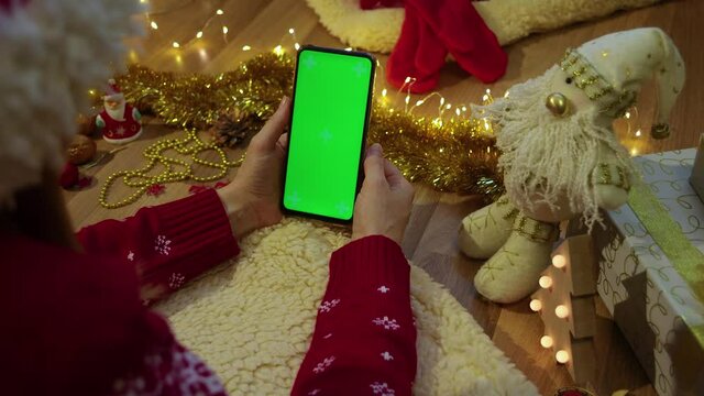 Woman hand holding phone in vertical mode, touching green screen, swiping photos. Christmas time concept. 