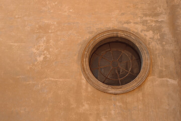 Fototapeta na wymiar Antique old round window with iron lattice framed on a beige brick wall in Europe