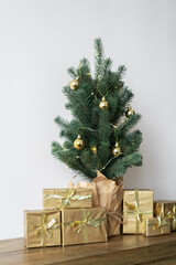 a small Christmas tree with warm bulbs in a pot on a wooden table with gifts wrapped in gold paper. the concept of Christmas