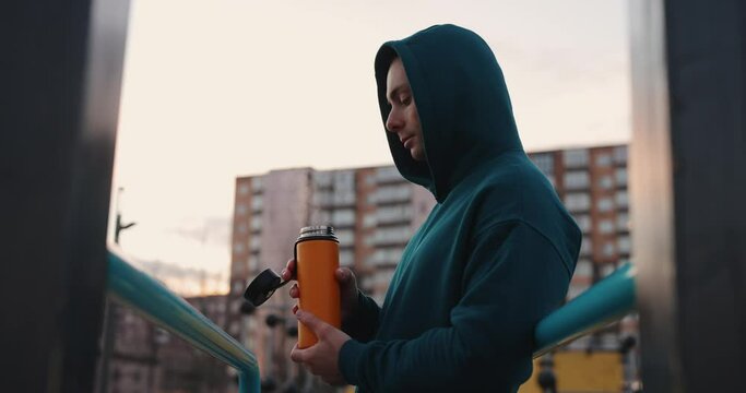 Man on the sports ground holding a thermos with hot tea and vapour, slow motion