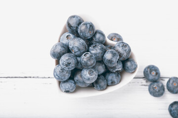 Blueberries in a plate of hearts on a white background. Fresh ripe blue berries. Love food concept. Top view, flat lay, copy space.