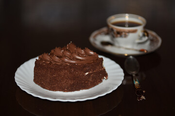 A piece of cake on a light plate with a cup of coffee and a beautiful spoon