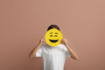 Little girl covering face with laughing emoji on pale pink background