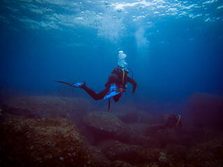 Scuba diver from behind. Diving in clear water. Rocks underwater. Underwater diving. Sardinia diving