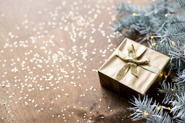 a golden gift box on a wooden table among fir branches with warm light bulbs