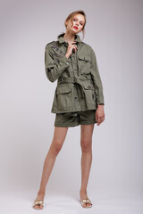 High fashion photo of a beautiful elegant young woman in a pretty green patterned jacket, short shorts posing over white, soft gray background. Slim figure. Studio Shot.