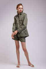 High fashion photo of a beautiful elegant young woman in a pretty green patterned jacket, short shorts posing over white, soft gray background. Slim figure. Studio Shot.