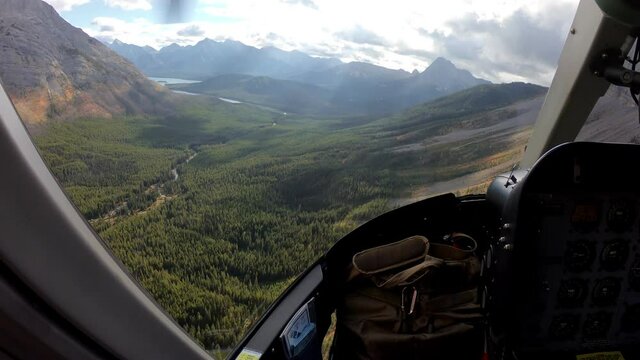 Inside of pilot flying a helicopter on autumn forest with turquoise lake in rocky mountains