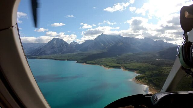 Inside of pilot flying a helicopter on autumn forest with turquoise lake in rocky mountains