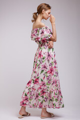 Fototapeta premium High fashion photo of a beautiful elegant young woman in pretty long dress with floral patterns in red color posing over white, soft gray background. Slim figure. Studio Shot. Femininity, tenderness