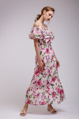 Naklejka premium High fashion photo of a beautiful elegant young woman in pretty long dress with floral patterns in red color posing over white, soft gray background. Slim figure. Studio Shot. Femininity, tenderness