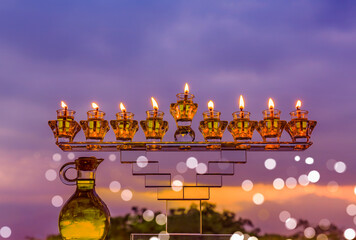Crystal festive menorah and burning candles with olive oil as symbol of Hanukkah - Jewish Holiday of Miracle Light. Blurred background of evening overcast sky and festive bokeh- 470100307